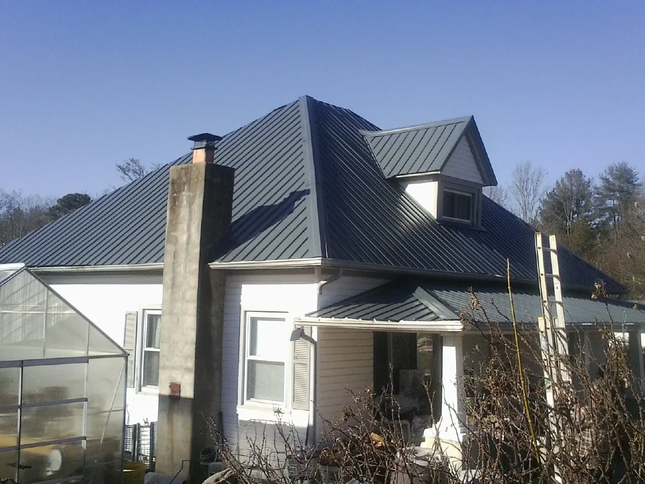 Dark blue standing seam metal roof on a white farmhouse with dormer — Slate & Tile Roof Repair by Roofing Brothers in Lowden