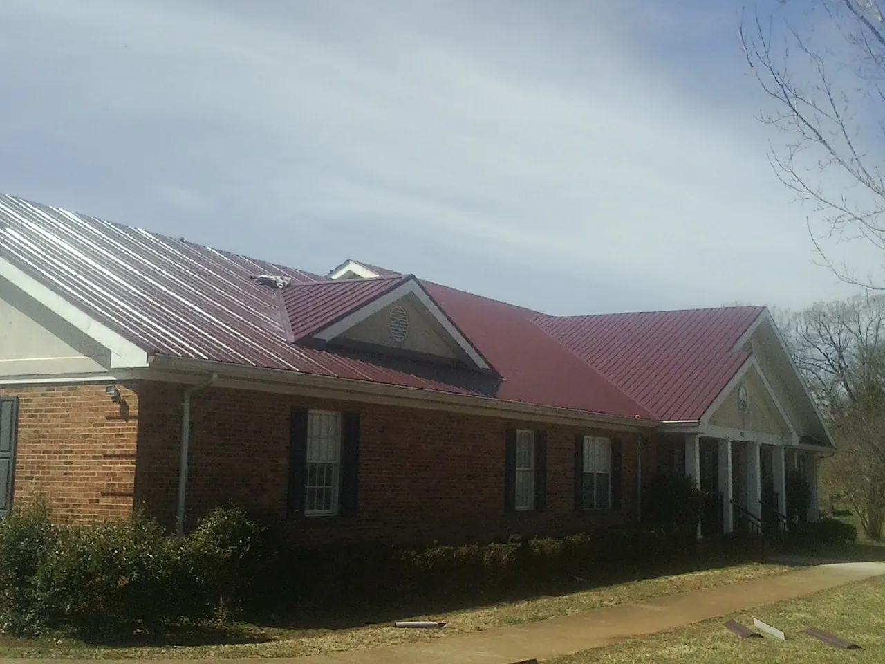 Red metal roof with gabled entries on a long brick building, from a Hail Damage Roof Repair job in Lowden