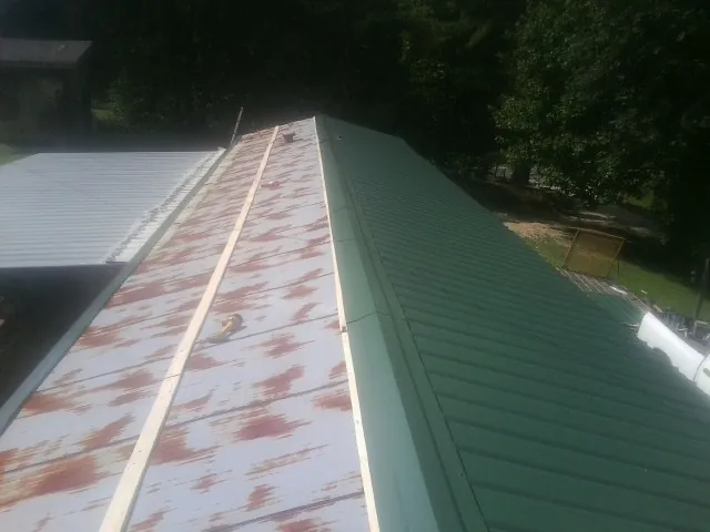 Old rusted panels beside newly installed green metal roofing — Wind Damage Roof Repair by Roofing Brothers in Lowden