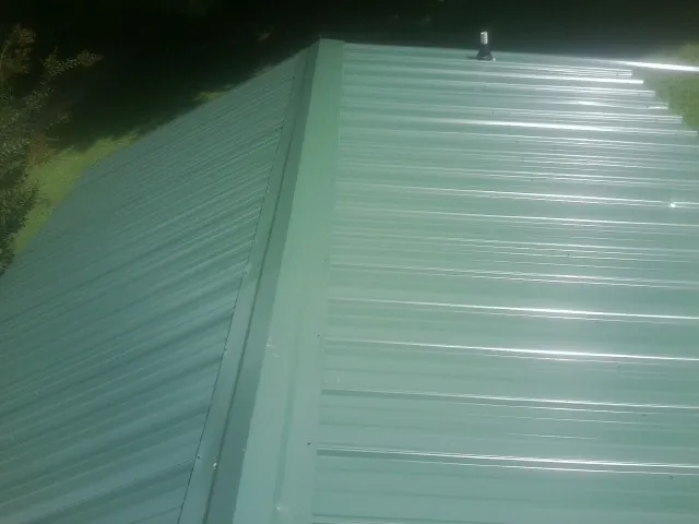 New green metal panels meeting at the ridge of a roof — Flat Roof Repair work by our crew in Lowden