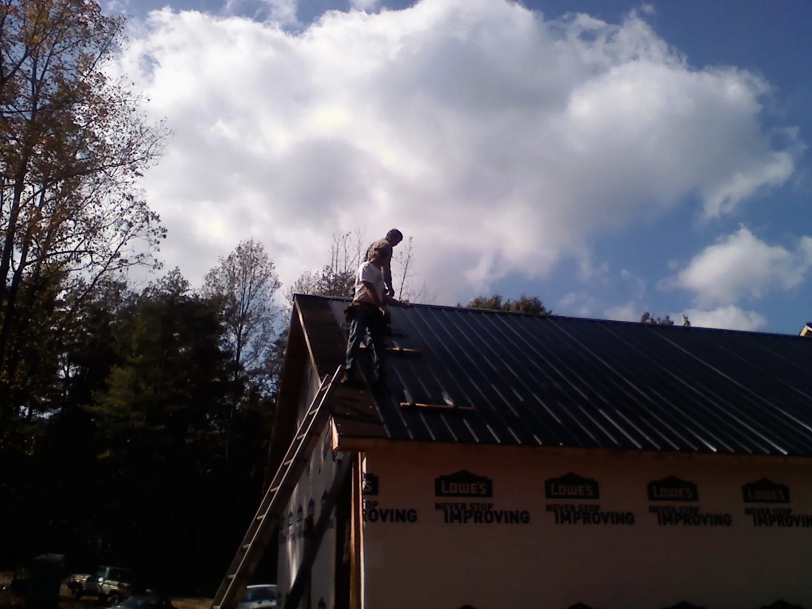 Roofer fastening dark metal panels high against a cloudy sky, from a Roof Inspection job in Lowden