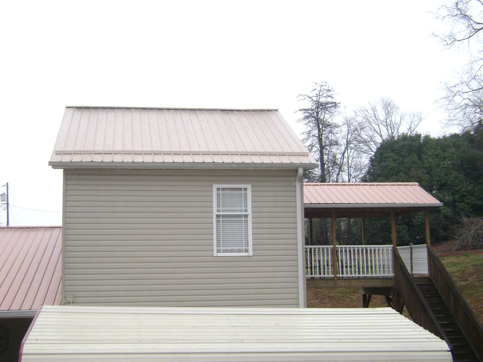 Tan metal roofs on a two story addition and attached porch, from a Roof Replacement job in Lowden